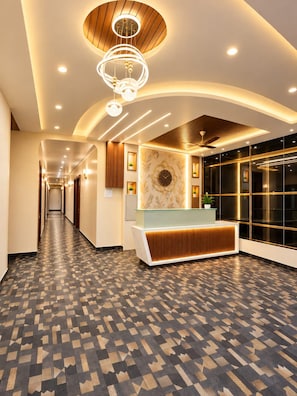 A hotel lobby with a reception desk, a patterned floor, and a ceiling with recessed lighting. - SRG Hotel and Restruant (Borgaon)