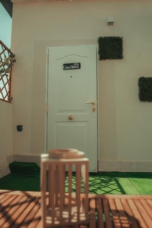 A white door with a sign above it, a small wooden stool in front, and a green mat on the floor. - La Siesta Hostel (Sagunto)