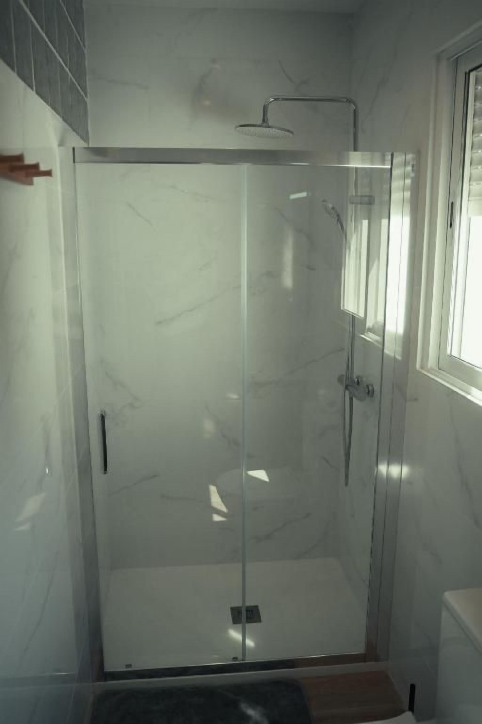 Un'area doccia vetrata con soffione a mano, porta in vetro e finestra sulla destra.
