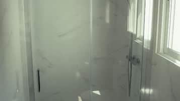 Un'area doccia vetrata con soffione a mano, porta in vetro e finestra sulla destra.