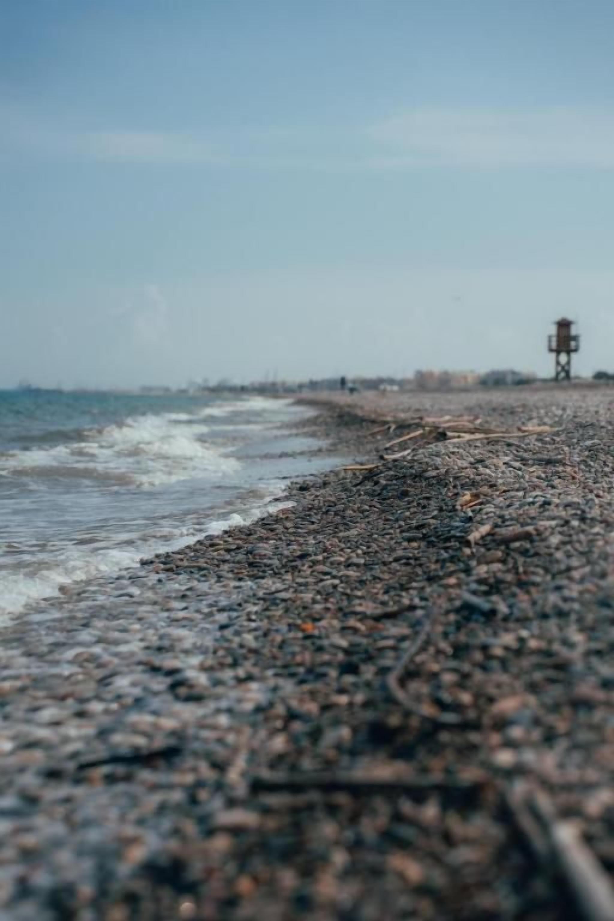 Uma praia de pedras com uma torre salva-vidas ao longe.