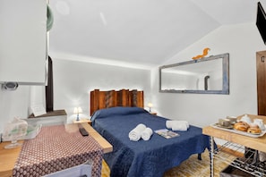Habitació d'hotel amb llit, taula de nit, làmpada i safata de petit esmorzar amb pastissos.