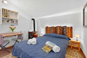 Habitació d'hotel amb un llit, una taula de treball, una cadira, una làmpada i un llibre damunt del llit.