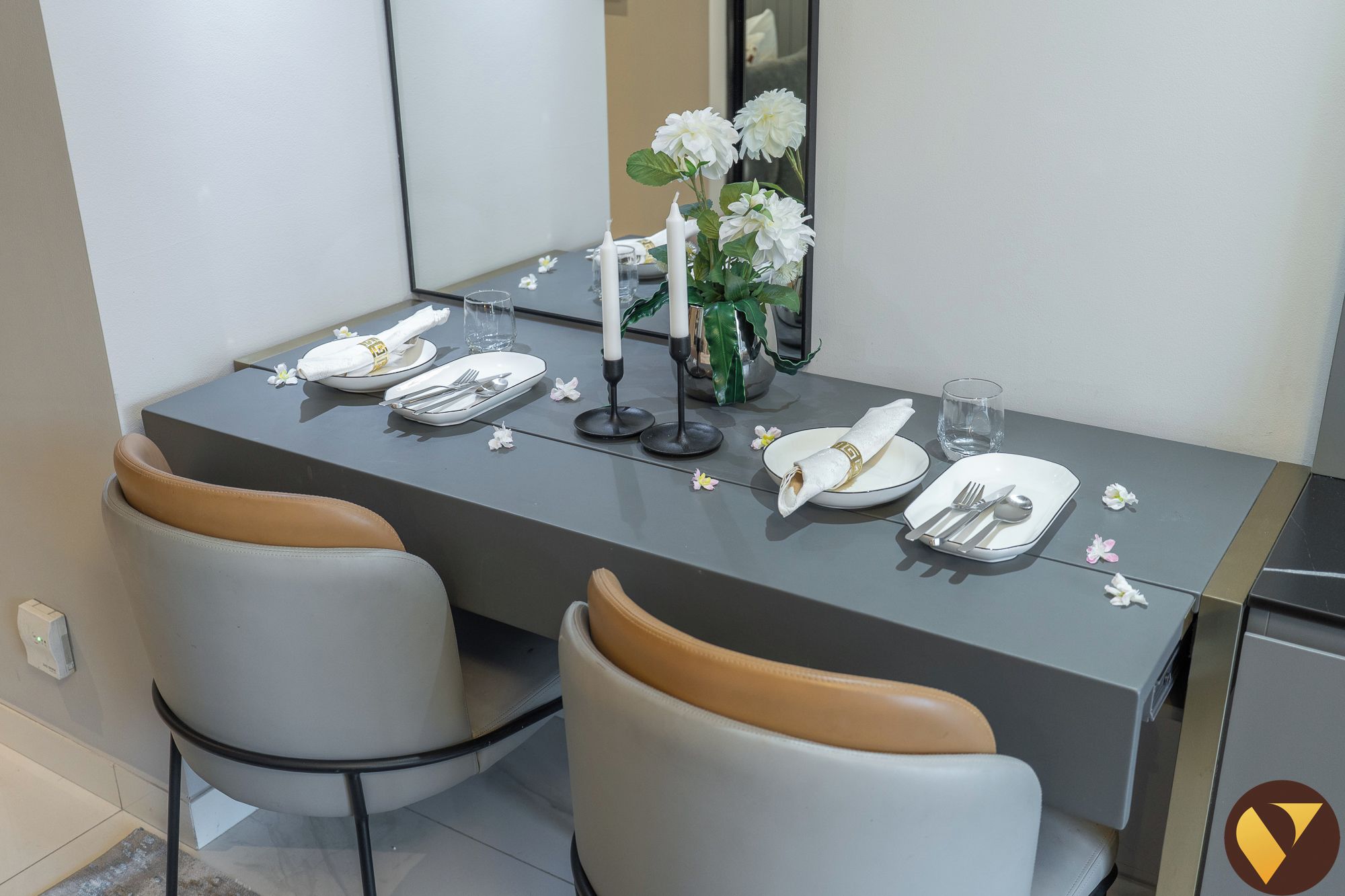 Une table à manger dressée avec de l’argenterie, des assiettes blanches et un vase rempli de fleurs blanches.