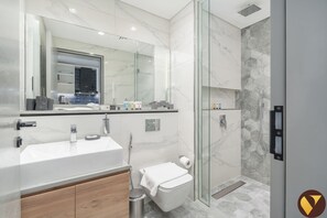 Une salle de bain moderne avec un grand miroir, un lavabo, des toilettes et une douche séparée par une paroi en verre.