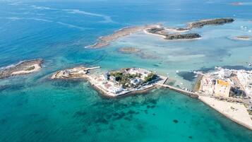 An aerial view of a coastal area with clear turquoise waters, several small islands, and a developed beachfront with buildings and a pier.