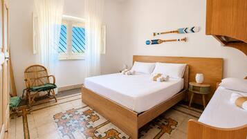 A hotel room with a wooden bed, a chair, a small table, and a window with curtains.