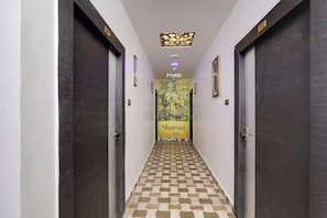 A hallway with dark wooden doors, a patterned floor, and a central wall with a mural. - Townhouse Hotel Vaishnavi Inn (Lucknow)