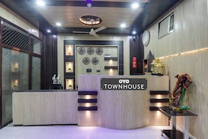 Een receptiebalie met een bord waarop 'OYO TOWNHOUSE' staat. Er hangen wandklokken, een plafondventilator en een beeld aan de muur.
