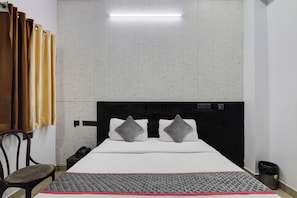 A hotel room with a bed, a chair, a bedside table with a phone, and a wall-mounted light. - Townhouse Hotel Vaishnavi Inn (Lucknow)