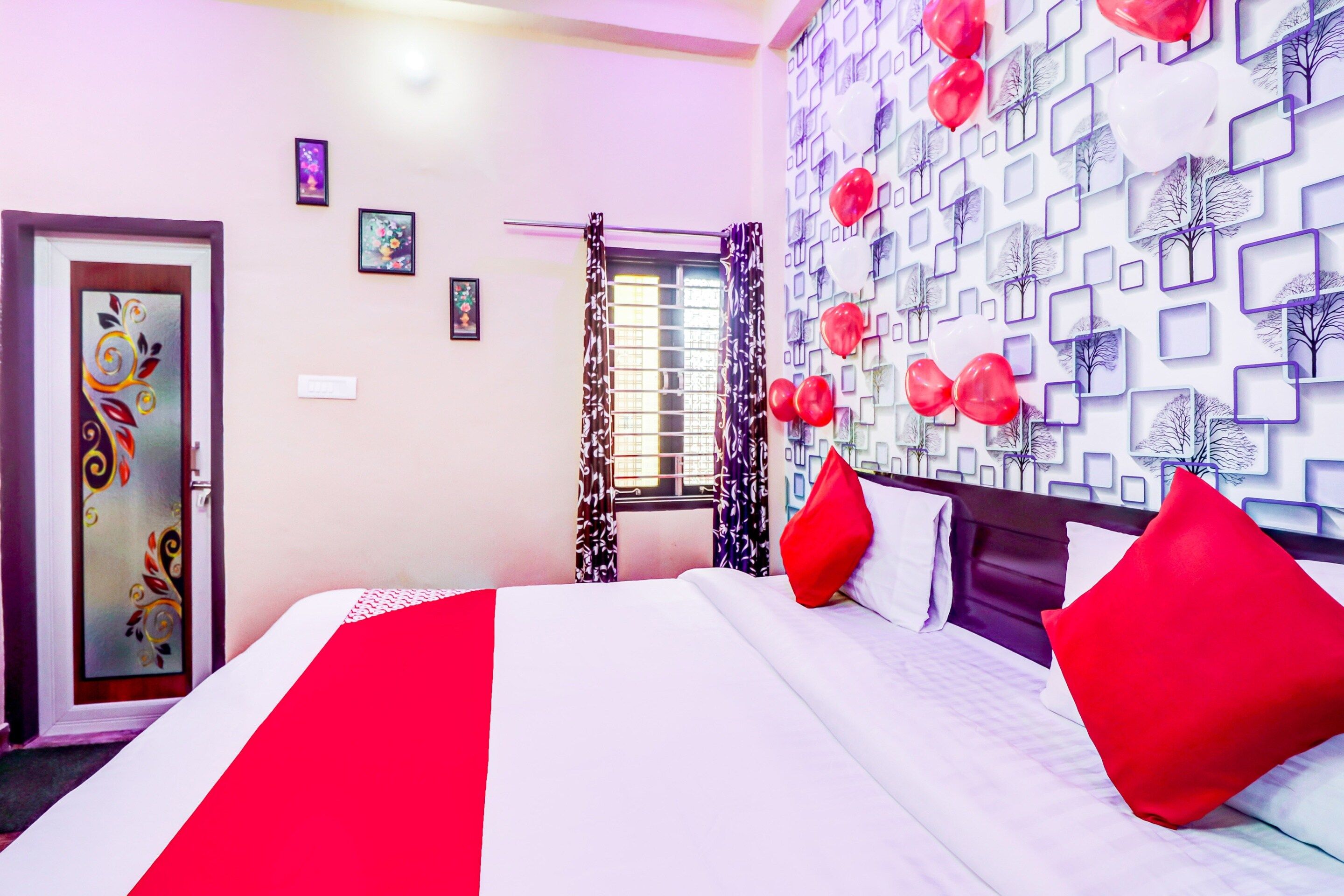 A hotel room with a bed, a door with decorative glass, a window with curtains, and a wall with a geometric pattern.