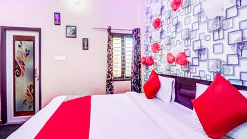 A hotel room with a bed, a door with decorative glass, a window with curtains, and a wall with a geometric pattern.