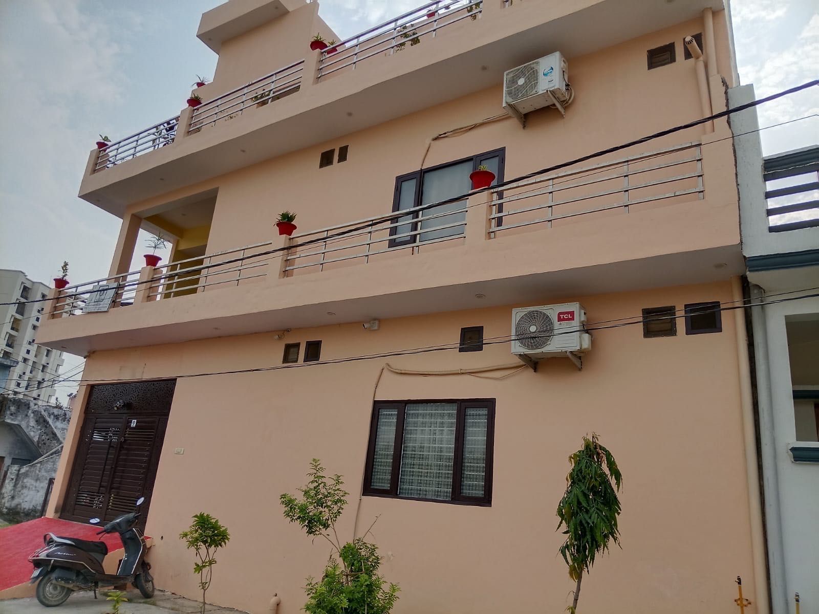 A multi-story building with balconies, air conditioning units, and a red scooter parked in front.