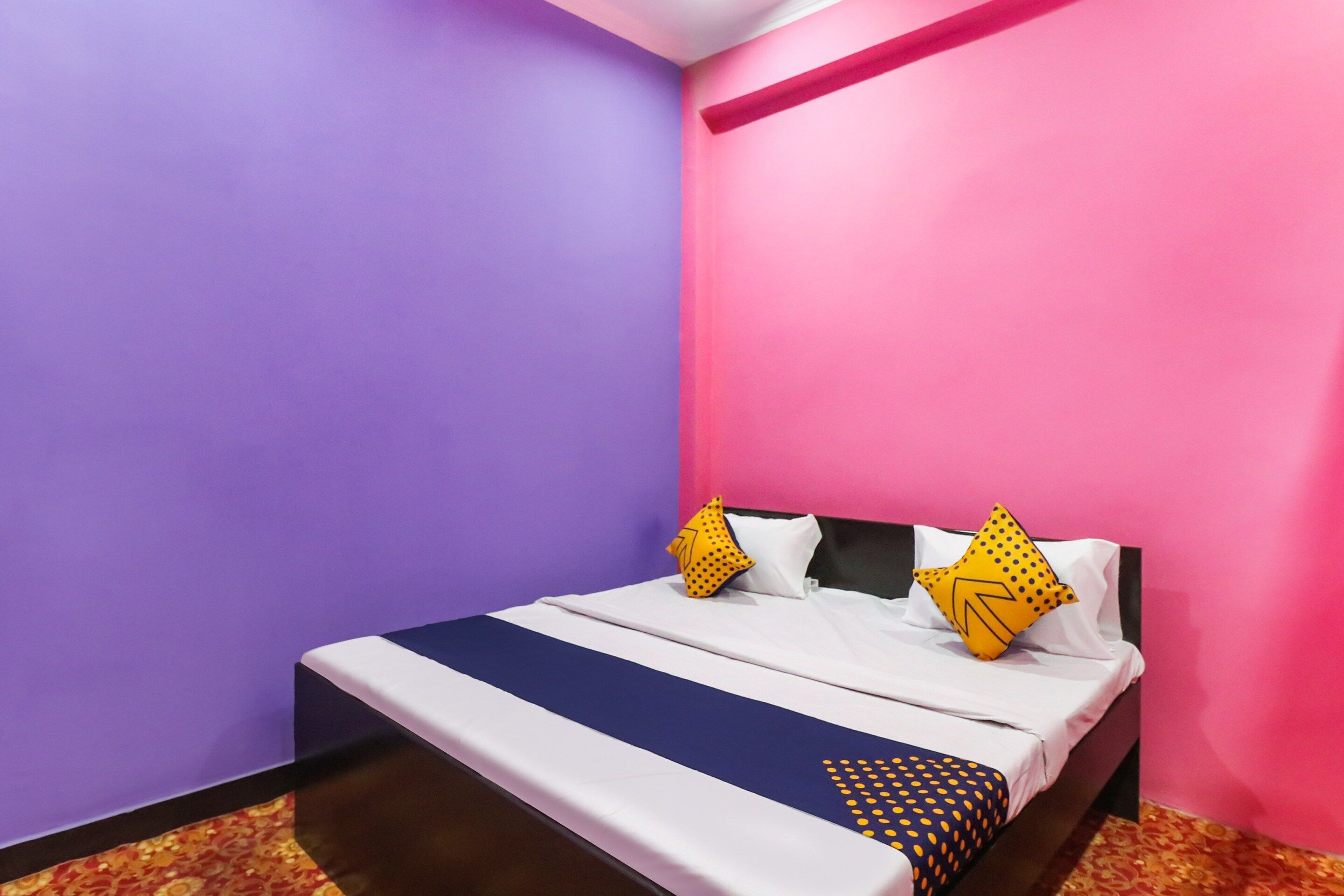 Un letto singolo con copripiumino bianco e blu a righe, due cuscini e una coperta decorata. Le pareti della stanza sono viola e rosa.