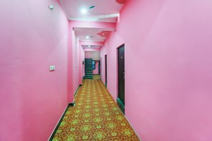 A corridor with pink walls and a patterned carpet, leading to a staircase and a door. - Hotel O by OYO Rajdhani Hotel (Lucknow)