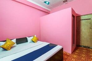 Una stanza con pareti rosa, un letto con lenzuola bianche e azzurre, e una porta in legno.