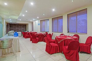Een feestzaal met verschillende ronde tafels, rode stoelen en een buffet.