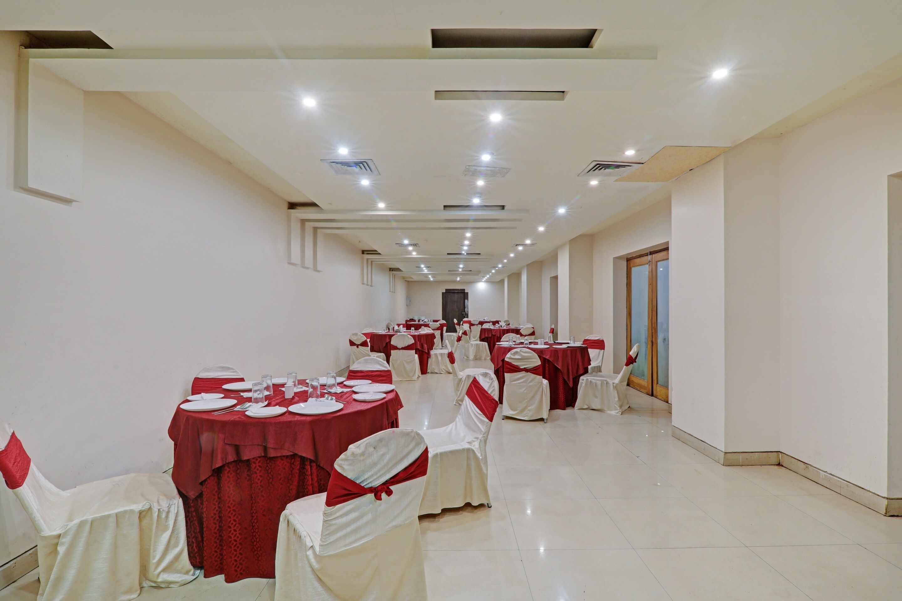 A banquet hall with multiple round tables, white chairs with red sashes, and a tiled floor.