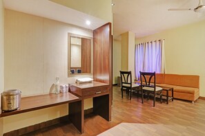 Een hotelkamer met een houten bureau, een spiegel, een bijzettafeltje, een bank en een eethoek met stoelen.