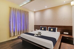 Een hotelkamer met een groot bed, nachtkastje, een lampje aan de muur en een raam met gordijnen.