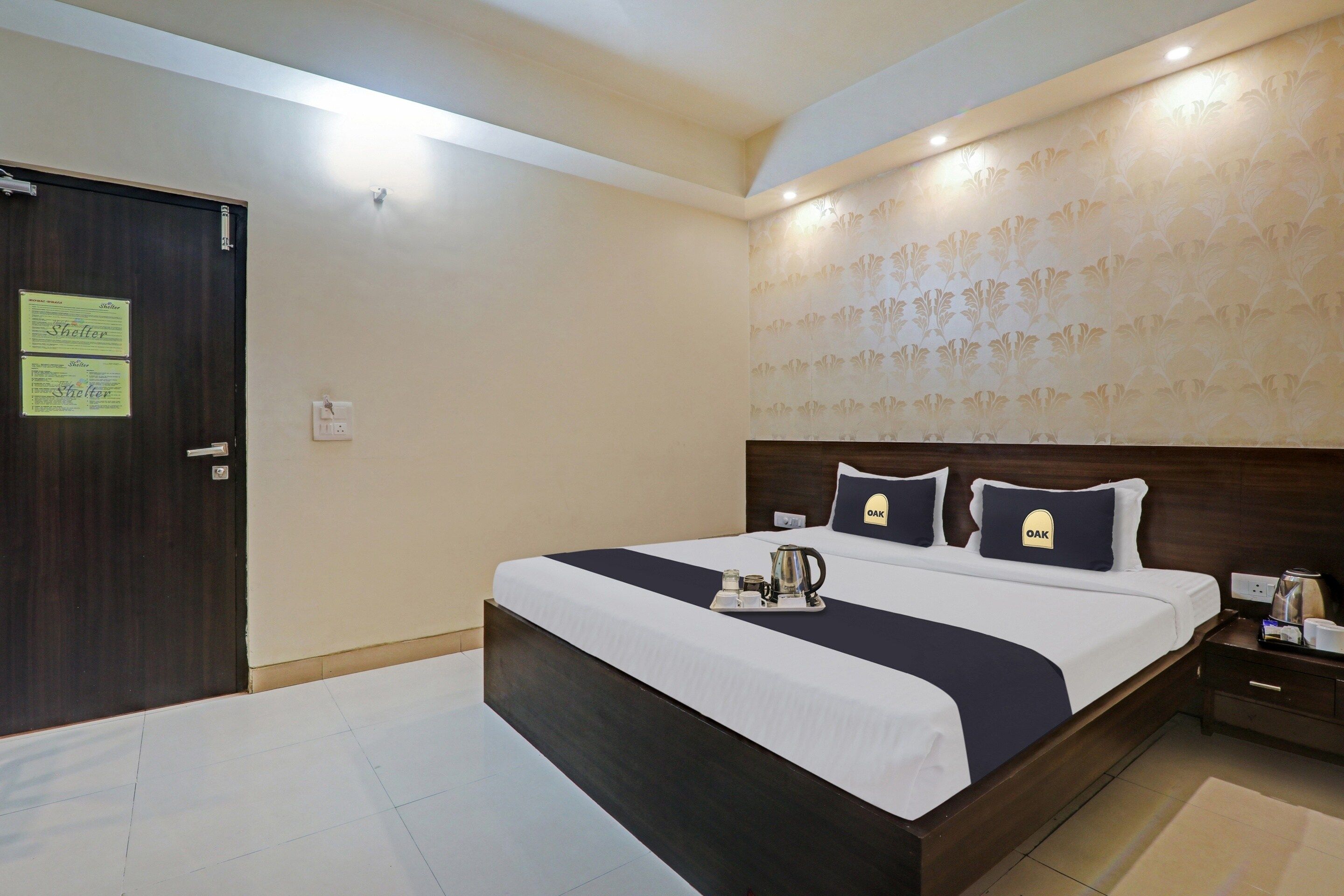 A hotel room with a large bed, a nightstand, and a wall-mounted lamp.