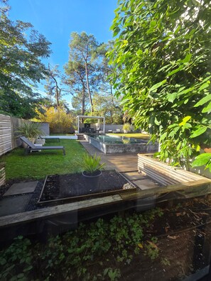 Un patio trasero con piscina, terraza de madera y zona de estar con sillones reclinables.