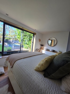 Quarto com uma cama grande, janela, espelho redondo e vista para o exterior.
