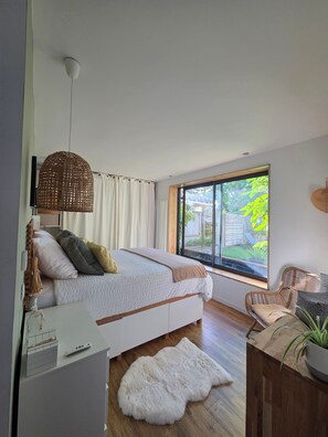 Quarto com cama, uma janela grande, luminária pendente e chão de madeira.