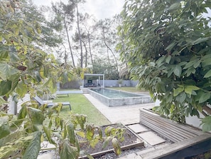 Patio trasero con piscina, zona de estar techada y jardín con diversas plantas.