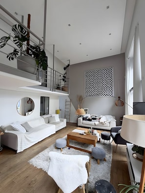 A modern living room with a white sofa, a wooden coffee table, and a patterned wall hanging. - Bed and Breakfast 'Maison Océâme - Chambre 2' with Shared Pool, Wi-Fi and Air Conditioning (Capbreton)