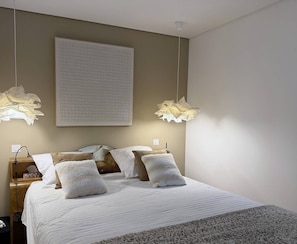 Quarto com cama, mesas de cabeceira, luminárias e iluminação embutida na parede.