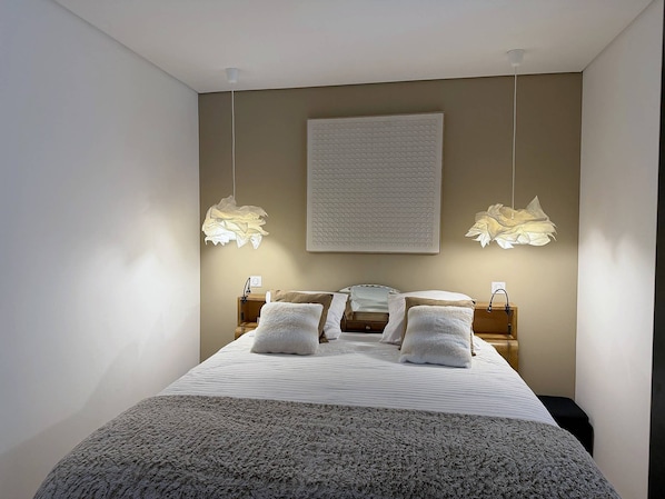 Quarto com uma cama grande, duas mesas de cabeceira, uma luminária na parede e um lustre no teto.