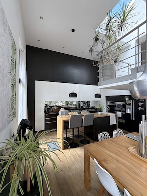 Cozinha moderna com armários preto e branco, mesa de jantar de madeira e plantas em vasos.
