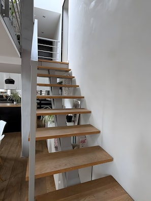 A modern interior with a wooden staircase, white walls, and a kitchen area visible in the background. - Guest Room 'Maison Océâme - Chambre 1' with Shared Pool, Wi-Fi and Air Conditioning (Capbreton)