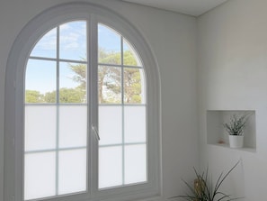 Una habitación con un amplio ventanal de arco, una pared blanca y un pequeño estante con una planta.