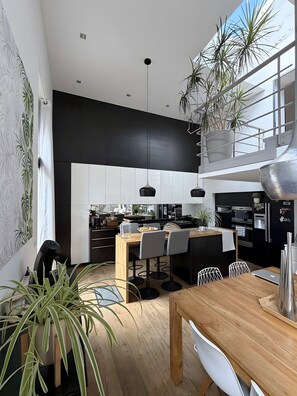 Cozinha moderna com armários preto e branco, mesa de jantar de madeira e plantas em vasos.