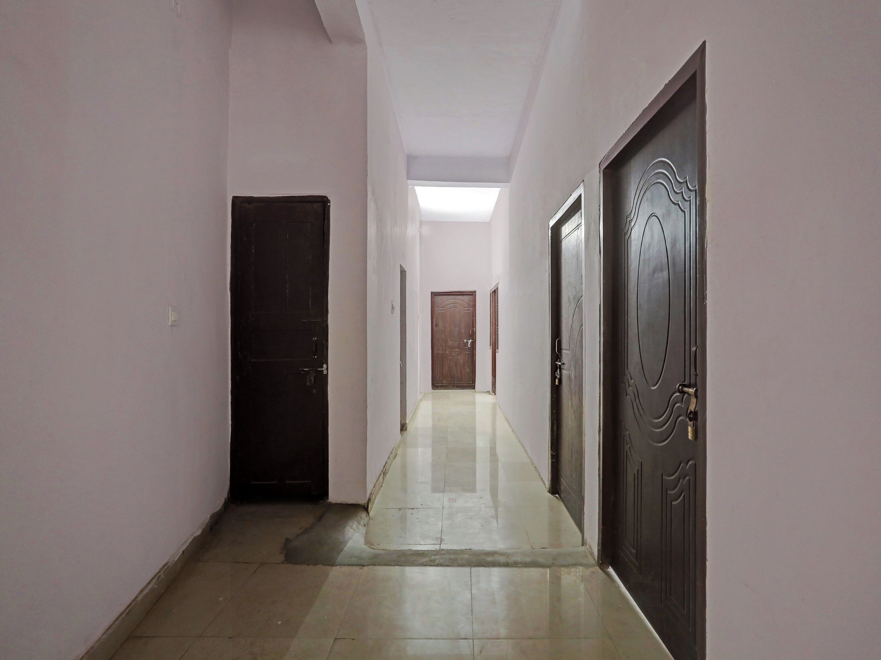 Un couloir avec des portes de chaque côté, un sol carrelé et un luminaire au plafond.