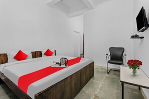 Een hotelkamer met een bed, een stoel, een klein tafeltje met een bloevas en een koffiezetapparaat op het nachtkastje.