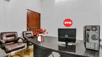 A room with a desk, two leather chairs, a computer monitor, a red logo on the wall, and a flower vase.