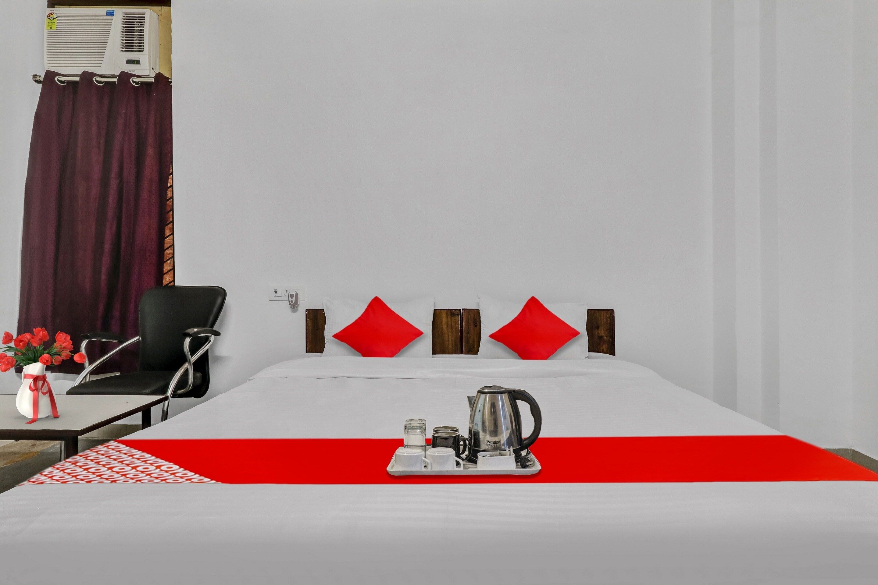 Una habitación de hotel con una cama, una silla, una mesa con una bandeja de desayuno y un jarrón de flores.