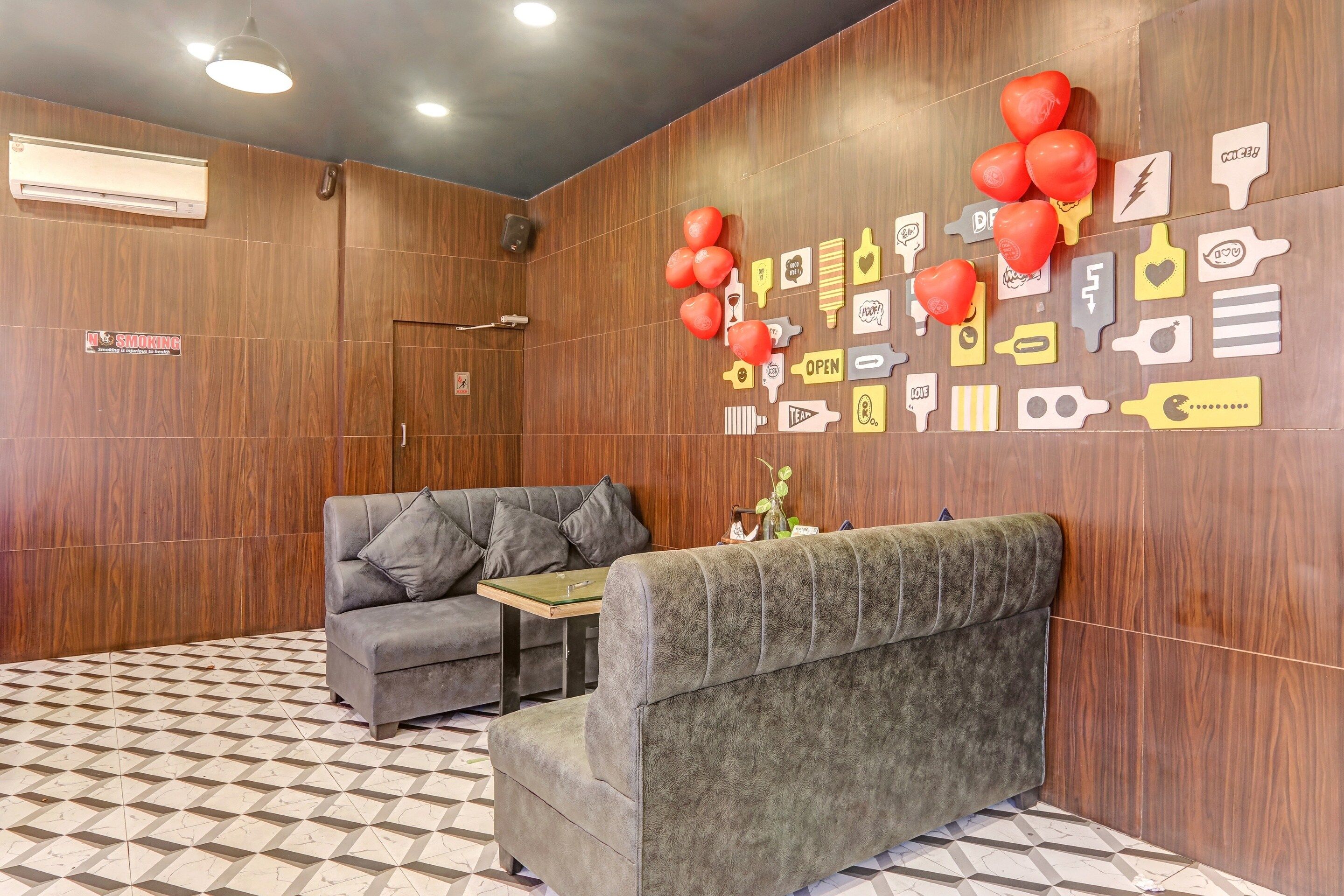 Un área de recepción con un sofá, una mesita y una pared decorada con varios carteles y globos.