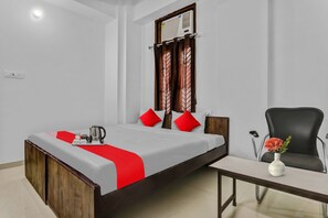 Een hotelkamer met een bed, een tafel, een stoel, een raam met gordijnen en een wandradiator.