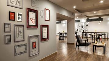 A modern interior with framed artwork on the walls, a dining area with tables and chairs, and a wooden floor.