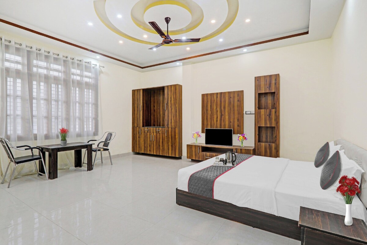 A modern hotel room with a bed, a desk, a chair, a TV, and wooden storage units.