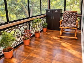 Un balcón con suelo de madera, plantas en macetas, una silla de madera y un mueble.