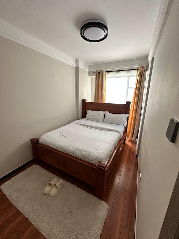 Una camera da letto con un letto di legno, un materasso bianco, un tappeto soffice e una lampada a sospensione al soffitto.