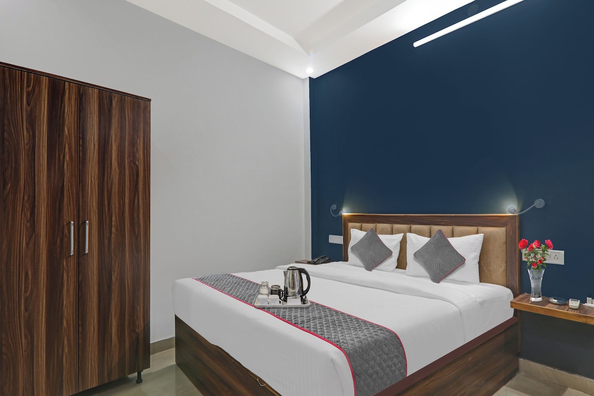 A hotel room with a wooden wardrobe, a bed with a quilted blanket, a bedside table with a vase of flowers, and a nightstand with a telephone.