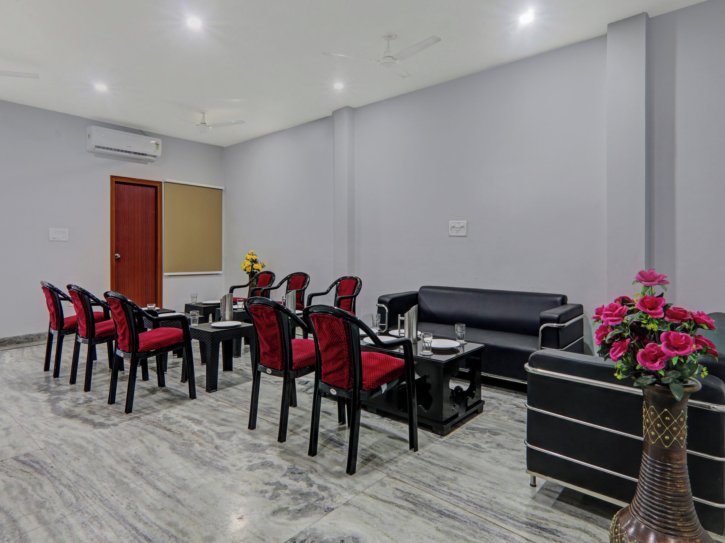 A conference room with a black sofa, red chairs, a black table, and a vase of flowers.
