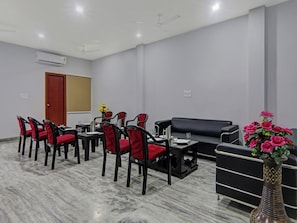 A conference room with a black sofa, red chairs, a black table, and a vase of flowers. - Townhouse swaroop inn (Lucknow)