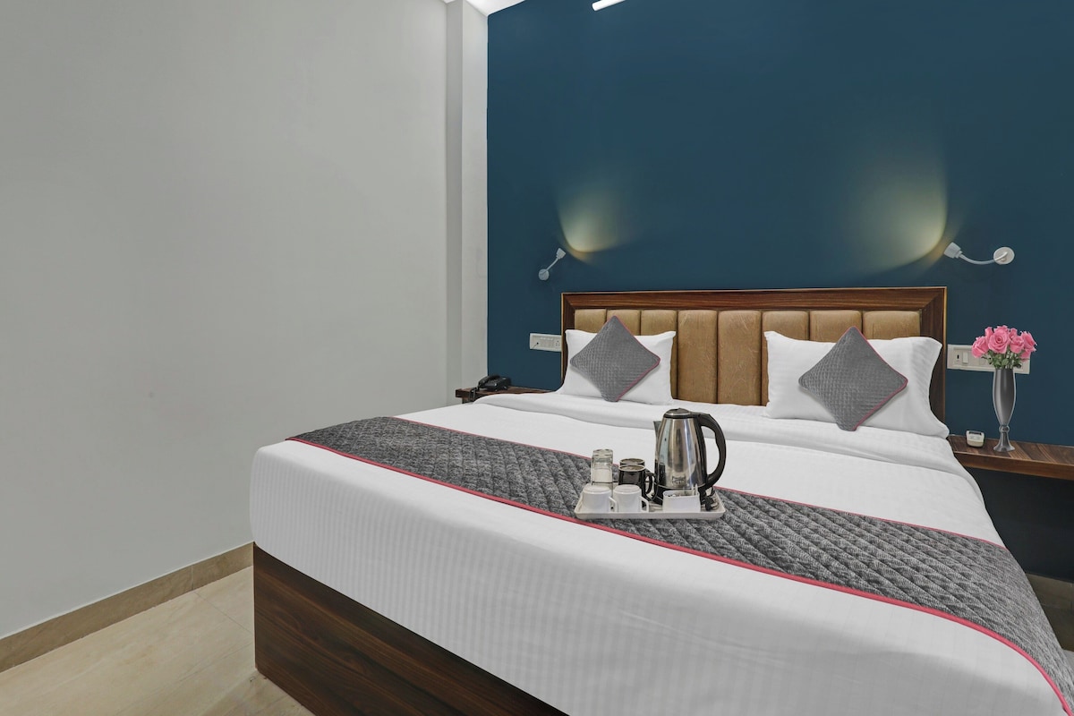 Habitación de hotel con cama, mesita de noche y una mesita auxiliar con un jarrón de flores.